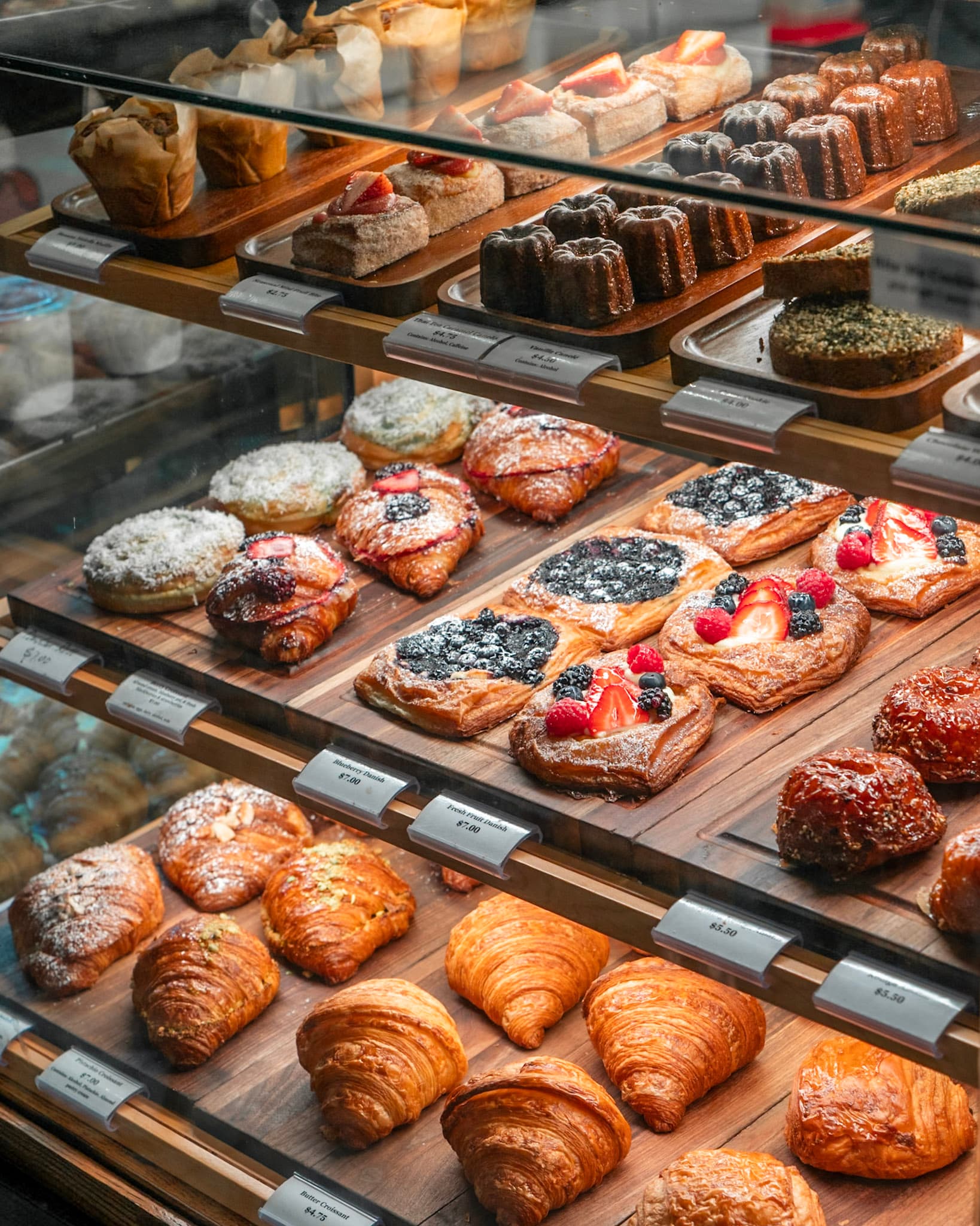 Full bakery display case with croissants, danishes, canelés and fruit tarts
